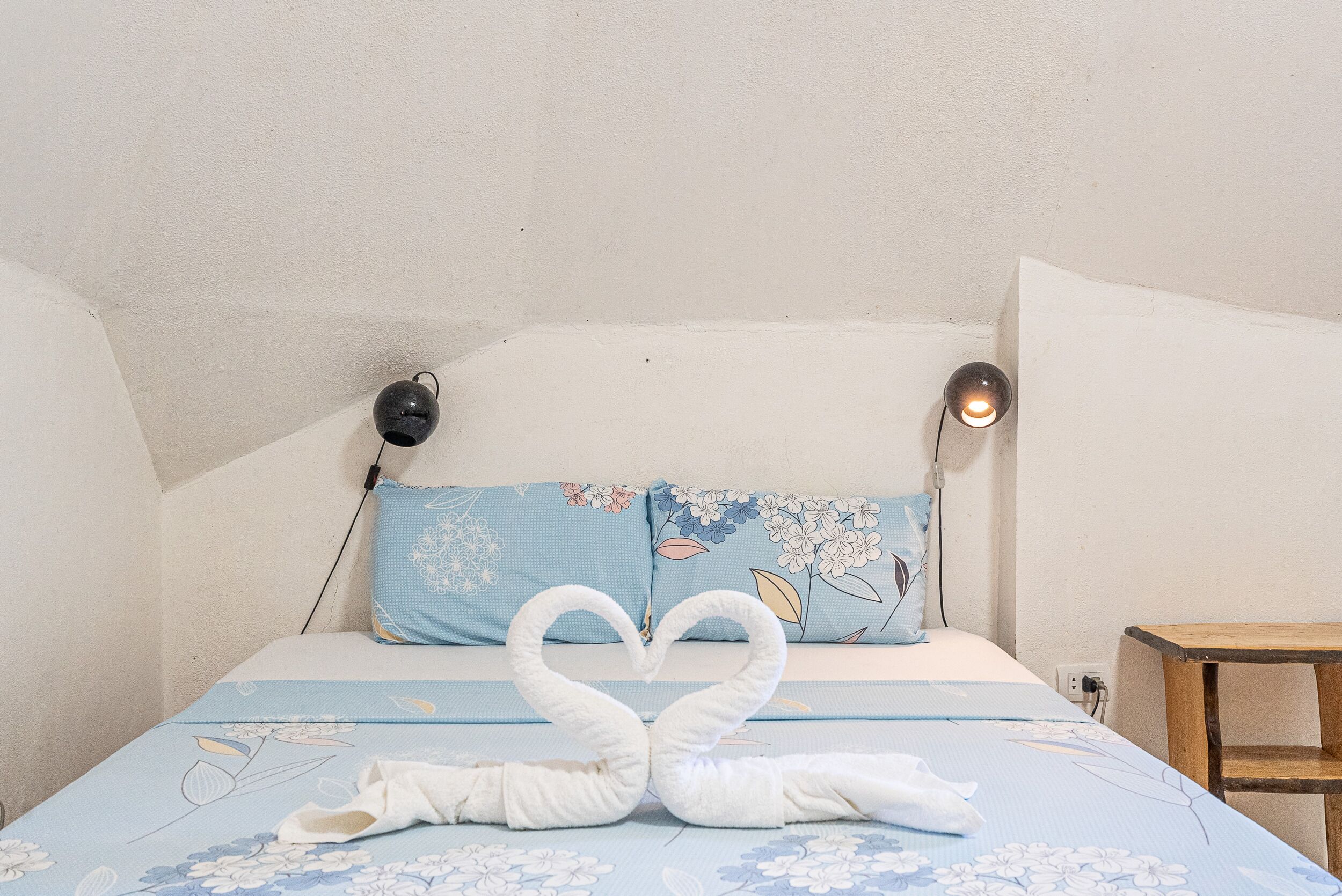Un lit recouvert d’une couvre-lit à motifs floraux bleus, des oreillers ornés de motifs floraux et deux serviettes blanches disposées en forme de cœur.