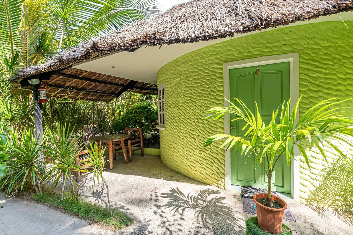 A thatched-roof structure with a green door, surrounded by lush tropical plants.
