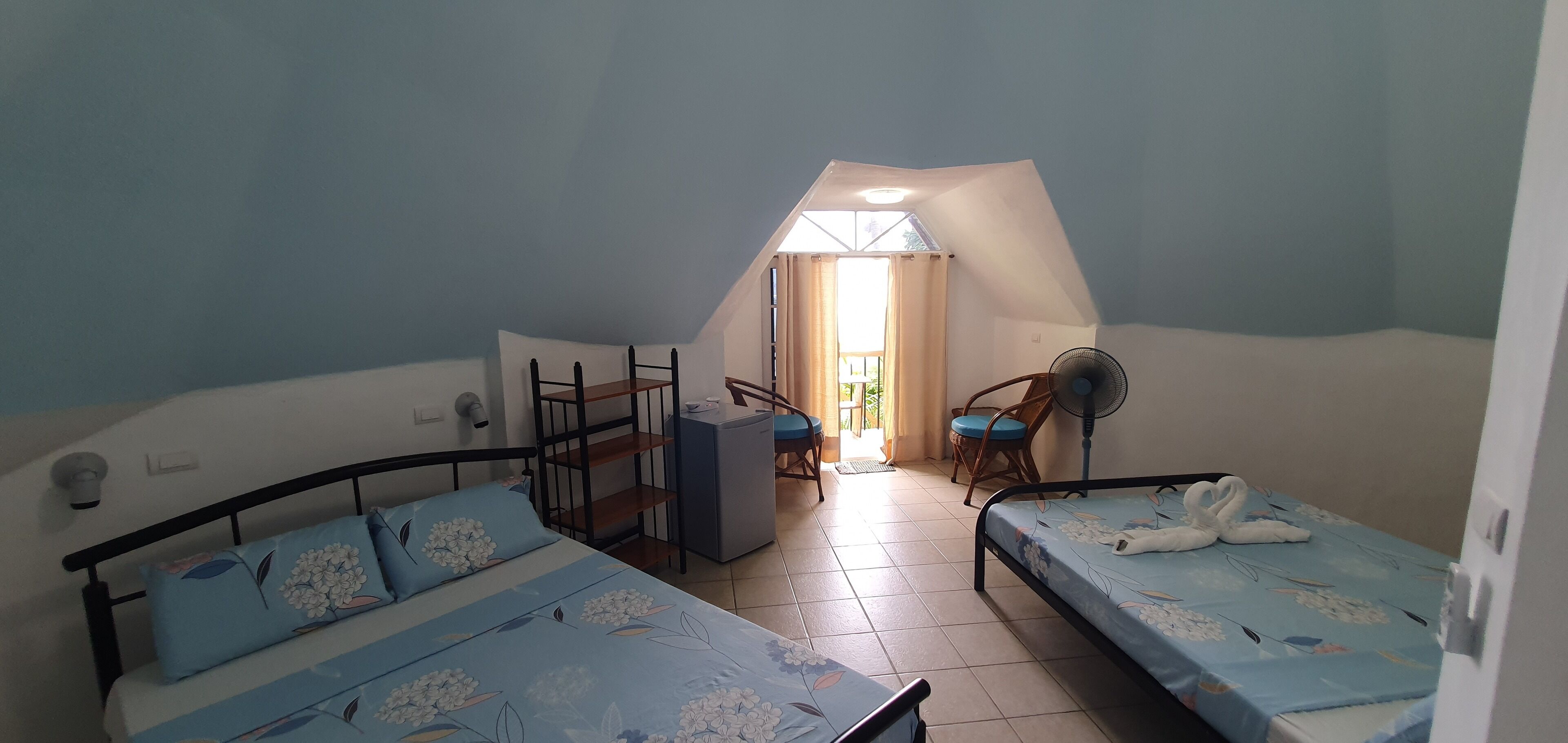 Un dormitorio con dos camas, un escritorio, una silla, un ventilador y una ventana con cortinas.