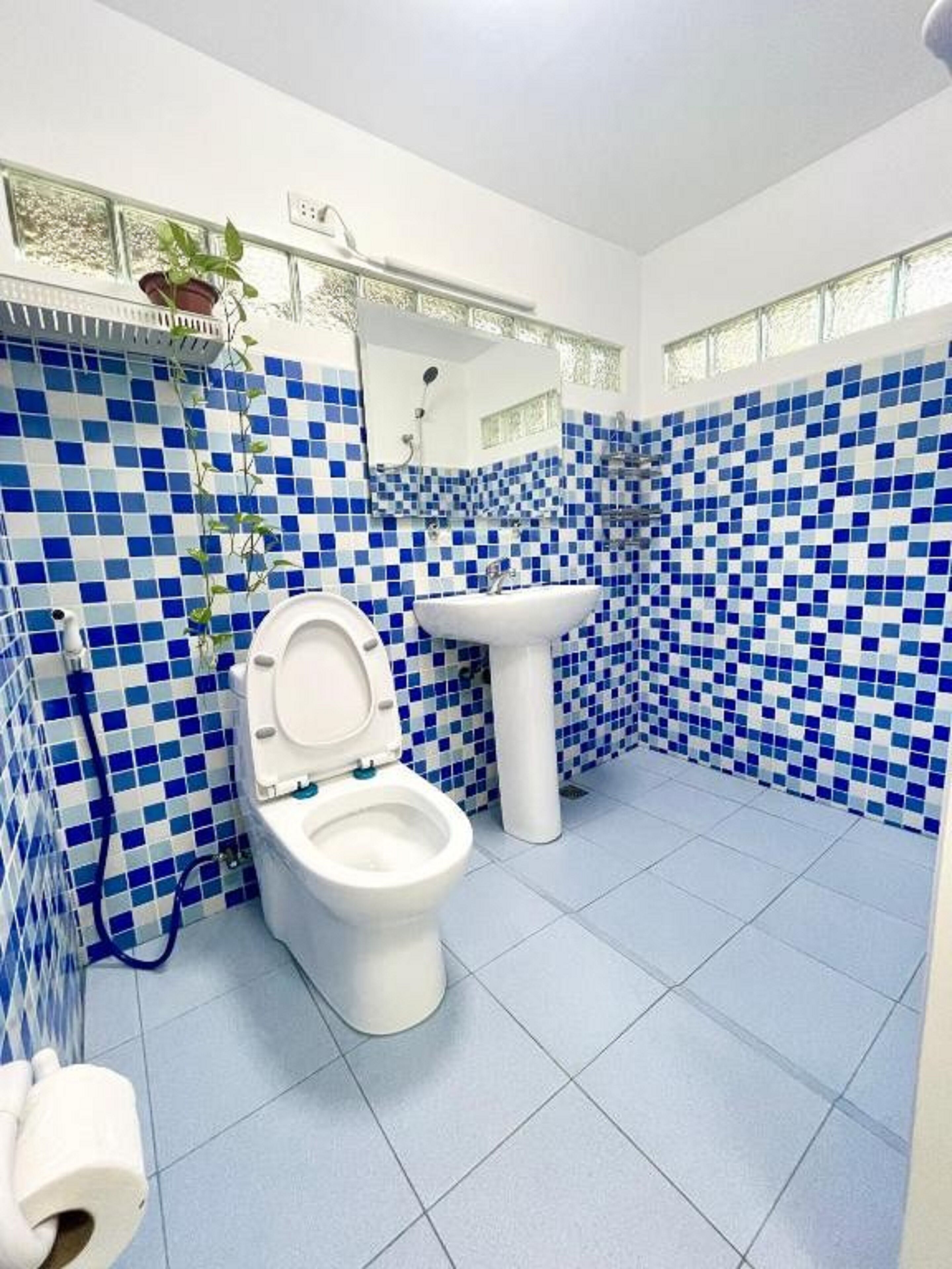 Une salle de bain avec des toilettes blanches, un lavabo blanc et des carreaux de mosaïque bleus sur les murs et le sol.