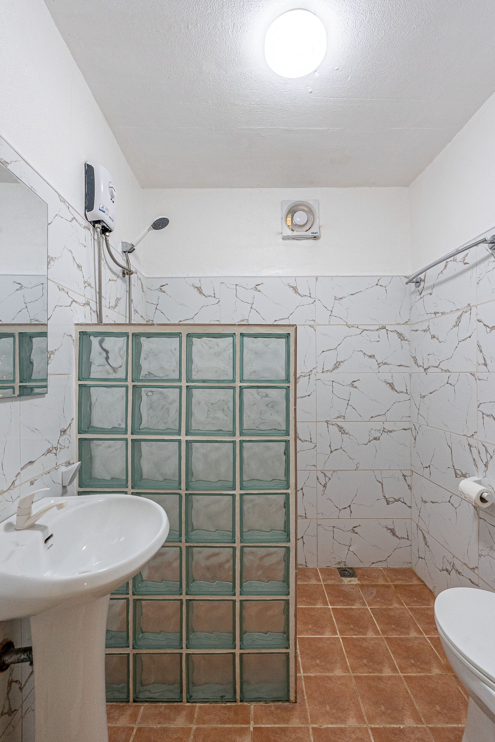 A bathroom with a white sink, a toilet, a shower with a glass door, and a ceiling light.
