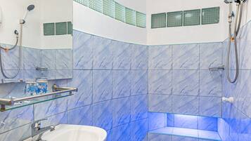 Un baño con un lavamanos blanco, un estante de vidrio, una ducha con cabezal de ducha manual y paredes cubiertas de azulejos azules.
