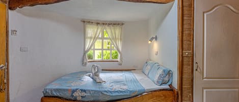 Un dormitorio rústico con una cama de madera, una ventana con cortinas y una puerta.