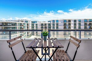 Ein Balkon mit Holztisch und Bänken, mit Blick auf einen modernen Gebäudekomplex.