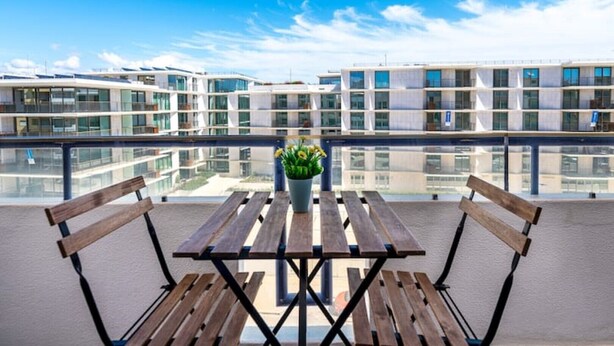 A balcony with a wooden table and chairs, a potted plant, and a view of modern buildings across the water. - Beachfront Apartment 4F - Armação de Pêra, Algarve (Armação)