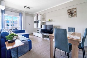 A modern living room with a sofa, a dining table with chairs, a TV, and a potted plant.