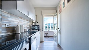 A narrow kitchen with modern appliances, a dining area with a view, and a balcony with a chair. - Beachfront Apartment 4F - Armação de Pêra, Algarve (Armação)