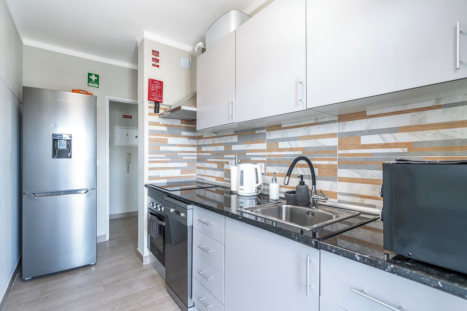 A modern kitchen with stainless steel appliances, a marble backsplash, and a black countertop.