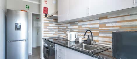 A modern kitchen with stainless steel appliances, a marble backsplash, and a black countertop.