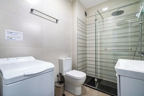 A modern bathroom with a glass shower enclosure, a toilet, and a washing machine.