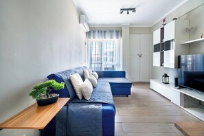 A modern living room with a blue sofa, a potted plant, and a television on a white stand.