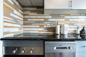Een moderne keuken met een roestvrijstalen afzuigkap, een inbouw vaatwasser en een decoratieve spatwand.