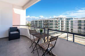 Un balcón con zona de estar, que incluye una silla y una mesa, con vista a un moderno complejo de edificios.