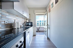 A modern kitchen with a black countertop, white cabinets, and a view to an outdoor balcony.