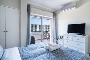 Ein Hotelzimmer mit Bett, Fernseher, Kleiderschrank und einem Balkon mit Blick auf Gebäude.