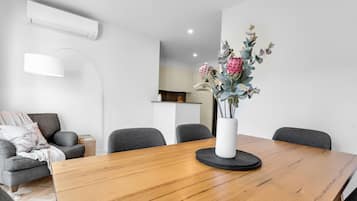 A modern dining area with a wooden table, grey chairs, a white vase with flowers, and a white pendant light.