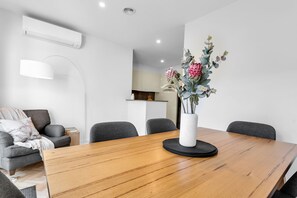 Un espace de salle à manger moderne avec une table en bois, des chaises grises, un vase blanc orné de fleurs et un luminaire suspendu blanc.