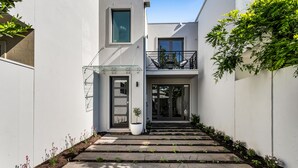 A modern house with a white exterior, a balcony with outdoor furniture, and a small garden area with stepping stones leading to the entrance. - Bev's Retreat by Ready Set Stay - peaceful retreat and close to all attractions. (South Yarra)