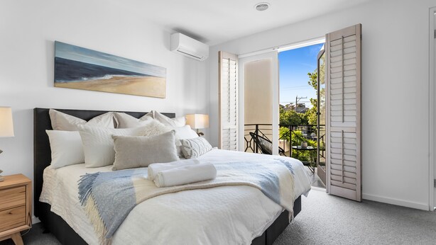 A bedroom with a large bed, a nightstand, a painting, an air conditioning unit, and a balcony with shutters. - Bev's Retreat by Ready Set Stay - peaceful retreat and close to all attractions. (South Yarra)