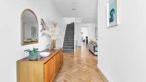 A hallway with a wooden herringbone floor, a wooden console table with decorative items, a mirror, and a staircase leading to another room. - Bev's Retreat by Ready Set Stay - peaceful retreat and close to all attractions. (South Yarra)