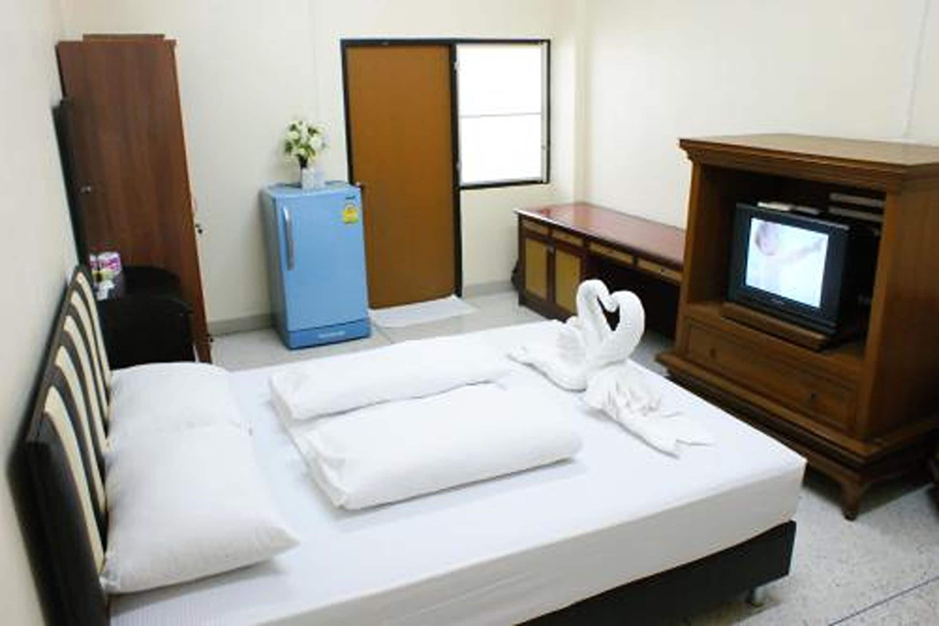 A hotel room with a bed, a small blue refrigerator, a wooden cabinet with a television, and a door with a window.