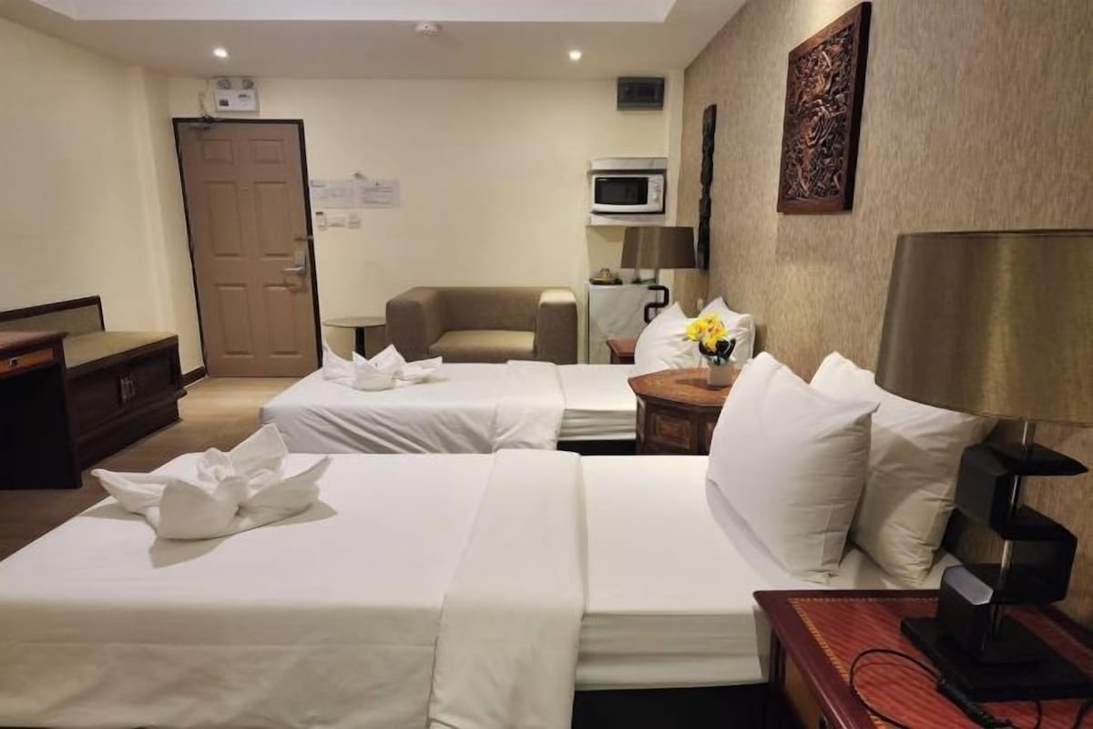A hotel room with two beds, a sofa, a microwave, a lamp, and a decorative wall piece.