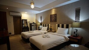 Ein Hotelzimmer mit zwei Betten, einem Schreibtisch, einem Stuhl, einer Lampe und einem kleinen Tisch.