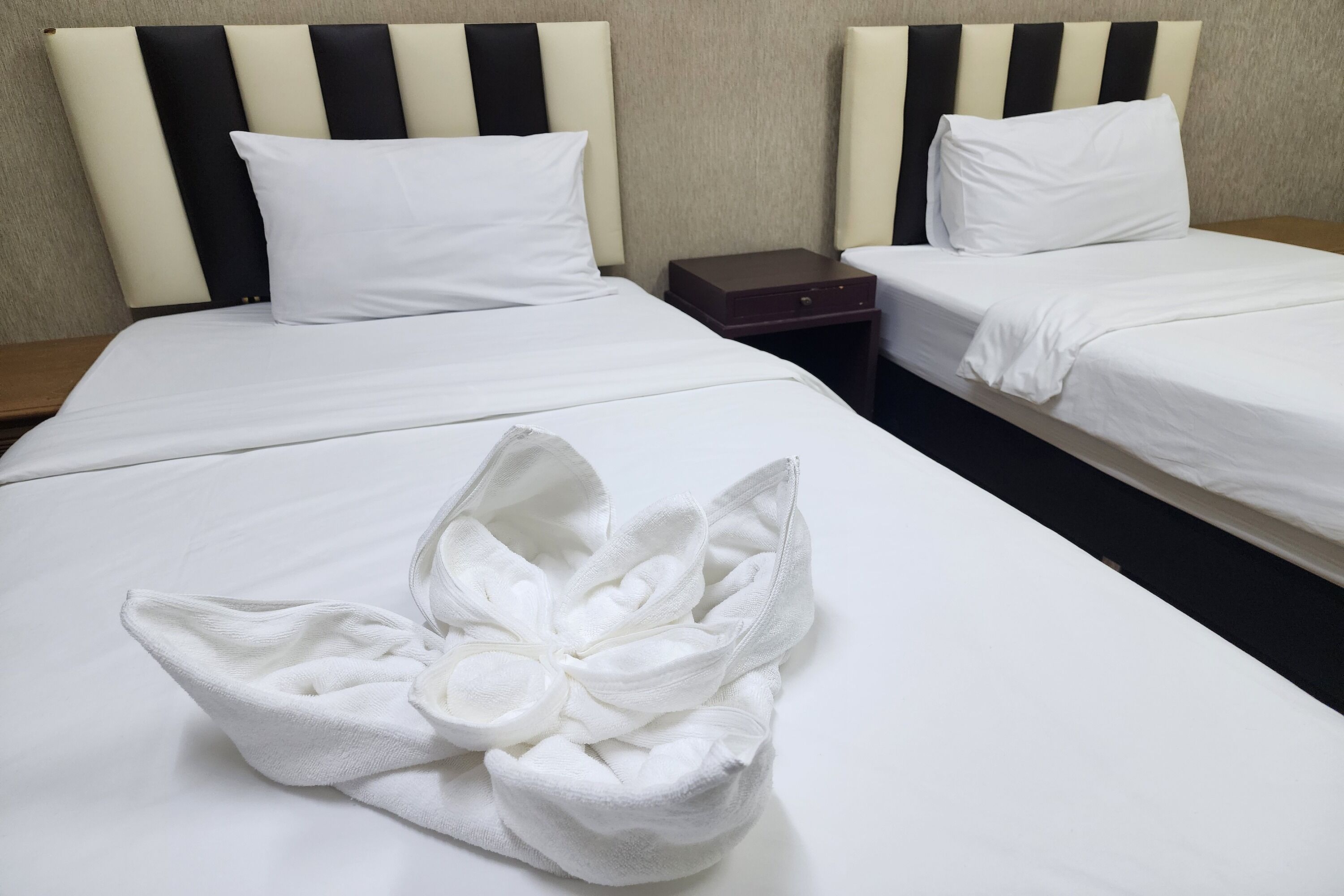 Habitación de hotel con dos camas, cada una con una almohada blanca y cabeceros a rayas negras y blancas. Hay una mesita de noche de madera entre las camas.