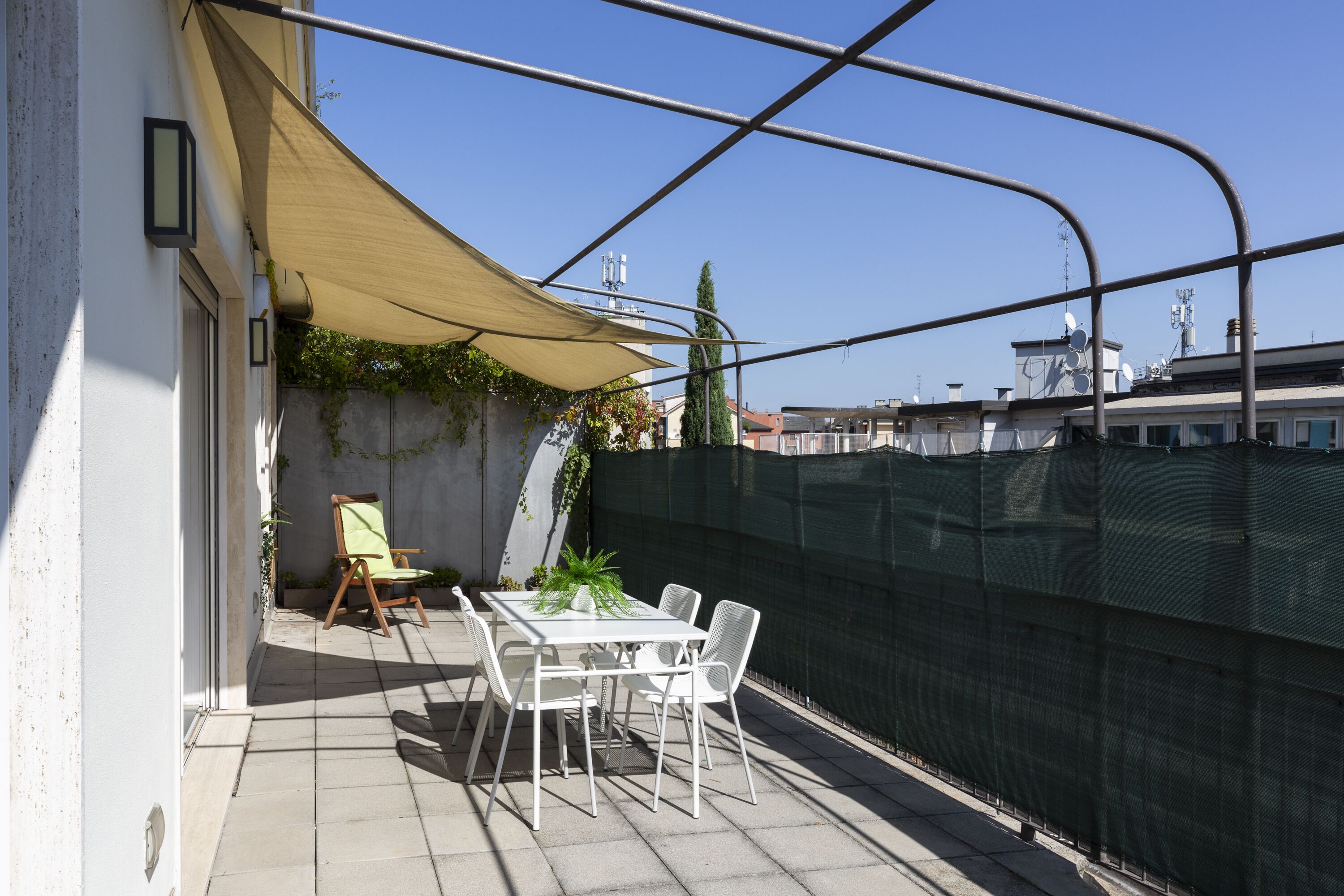 En tagterrasse med et bord og stole, en potteplante og en gul markise.