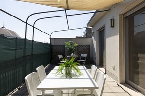 A patio with a table and chairs, a potted plant, and a green fence. - notaMi - Edolo Terrace (Milan)