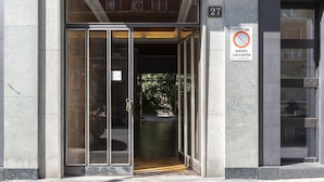Entrada de um edifício com porta de vidro, placa de proibido estacionar e o número 27 na parede.