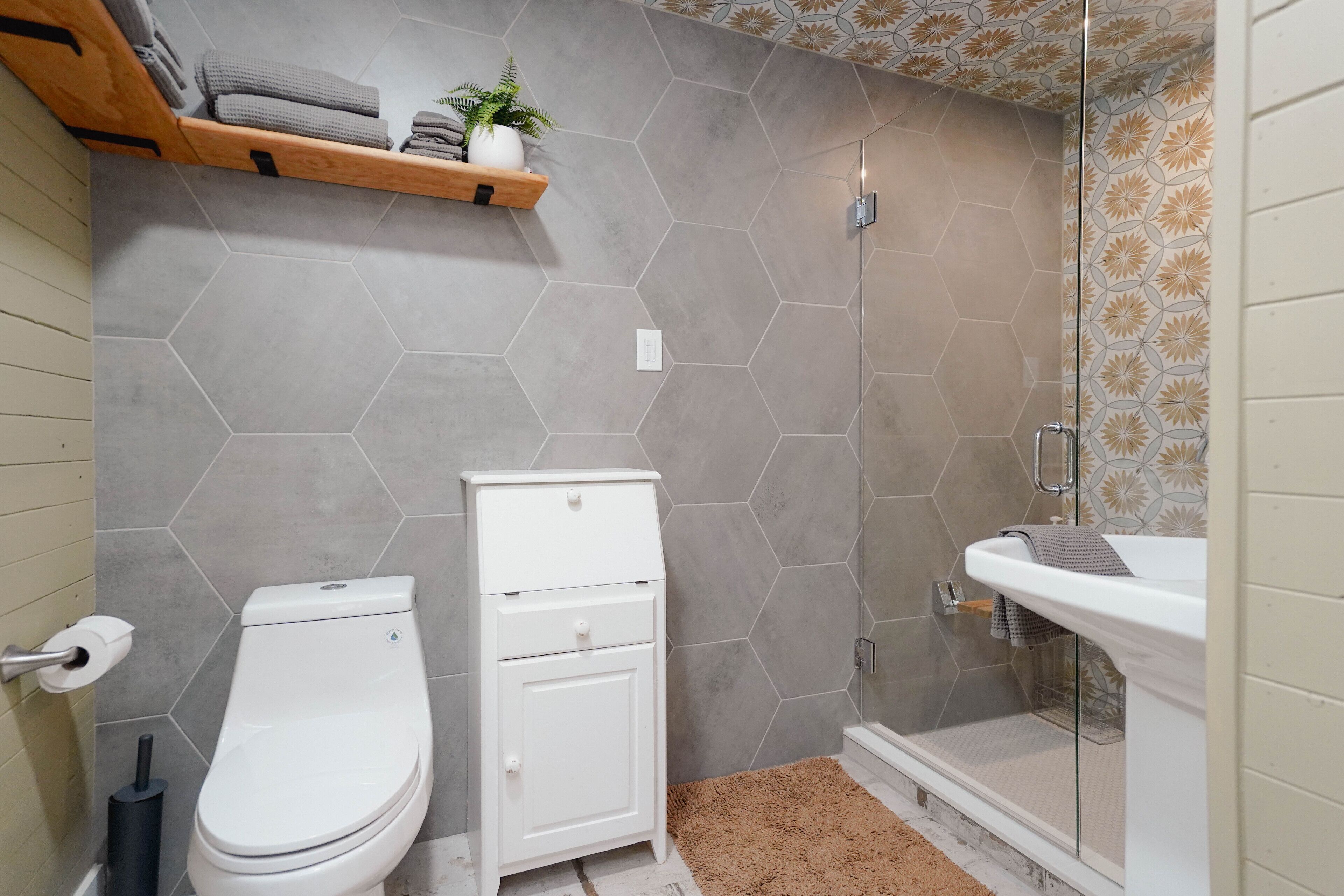 Et badeværelse med toilet, skab, bruser med glasdøre og vask.