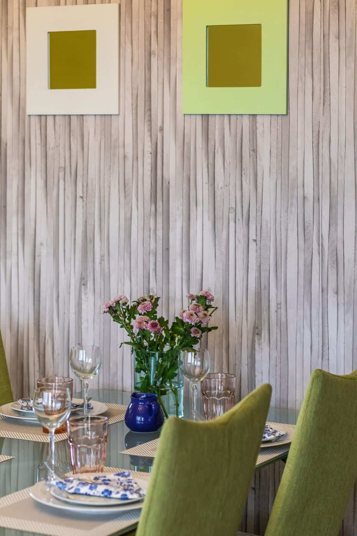 Ein Esstisch, gedeckt mit Tellern, Gläsern und einer Blumenvase, vor einer Holzwand mit gerahmten Bildern.