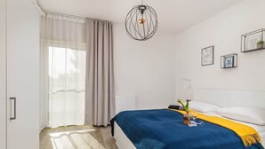 Un dormitorio con cama, mesita de noche, lámpara colgante y ventana con cortinas.