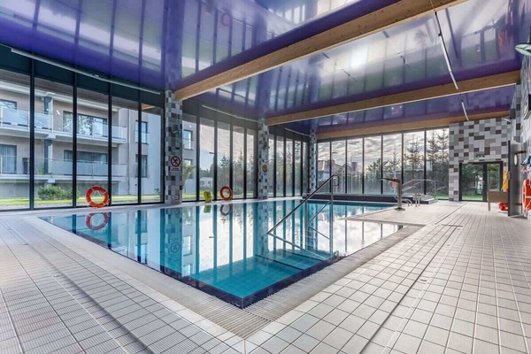 An indoor swimming pool with glass walls, lounge chairs, and modern architecture.