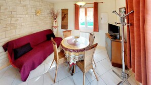 Una sala de estar acogedora con un sofá rojo, una mesa redonda de comedor con sillas, un televisor y un perchero.