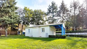 Una casita de una sola planta, con fachada blanca y detalles azules, rodeada de un césped cuidado y árboles.