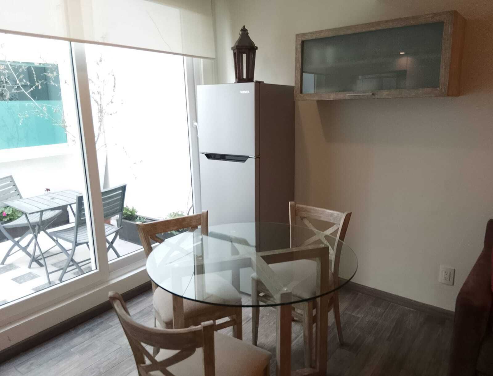 A compact kitchen with a glass table, wooden chairs, a white refrigerator, and a hanging lantern.