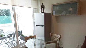 A compact kitchen with a glass table, wooden chairs, a white refrigerator, and a hanging lantern.