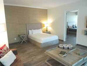 Et hotelværelse med en seng, et natbord, en lampe og et lille bord med en bog og kurve.