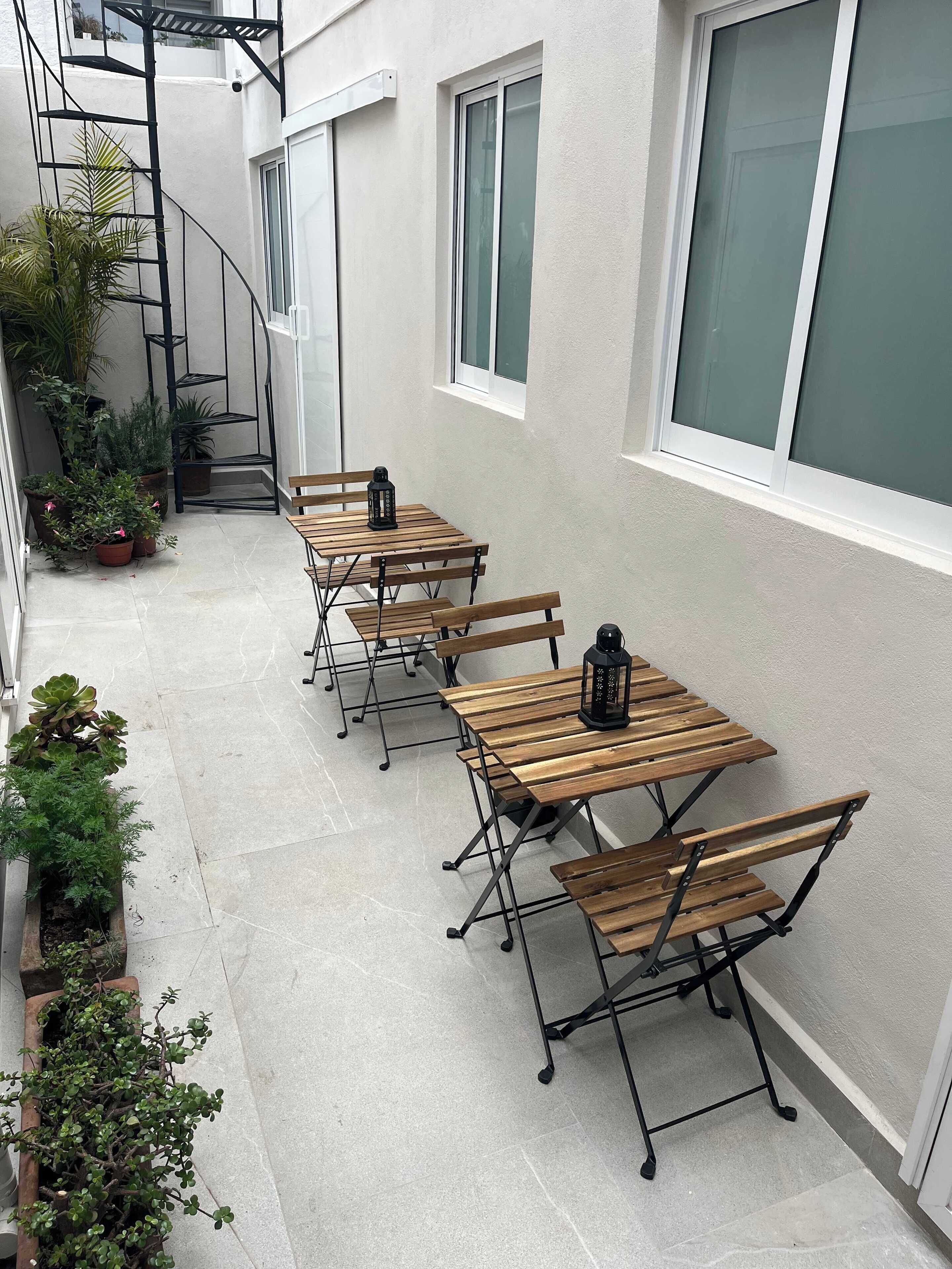 Eine kleine Terrasse im Freien mit Holztischen und -stühlen, Blumentöpfen und einer Metall-Wendeltreppe.