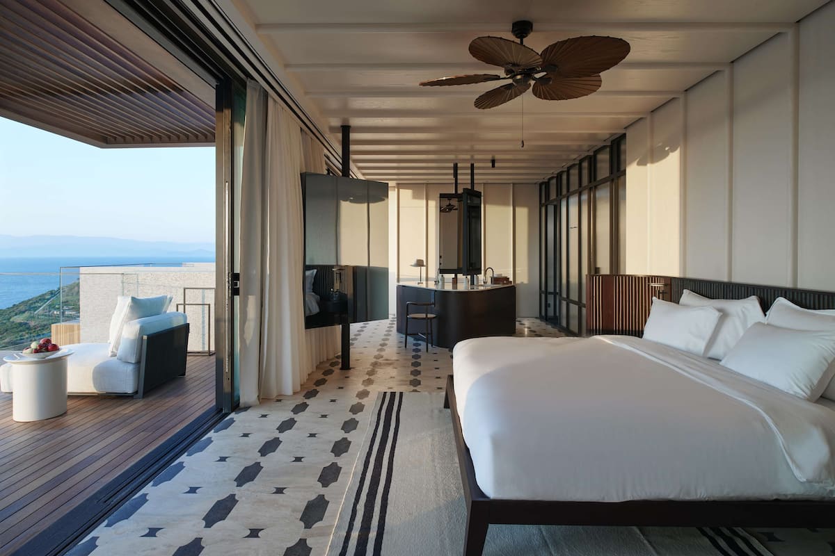 A modern hotel room with a large bed, a balcony with a view, a desk, and a ceiling fan.