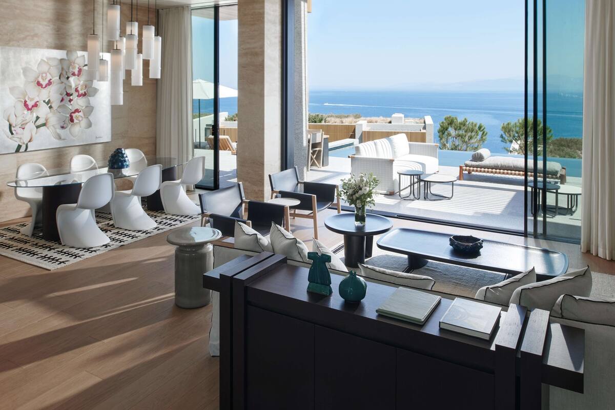 A modern hotel room with a large balcony, a dining area, and a view of the sea.