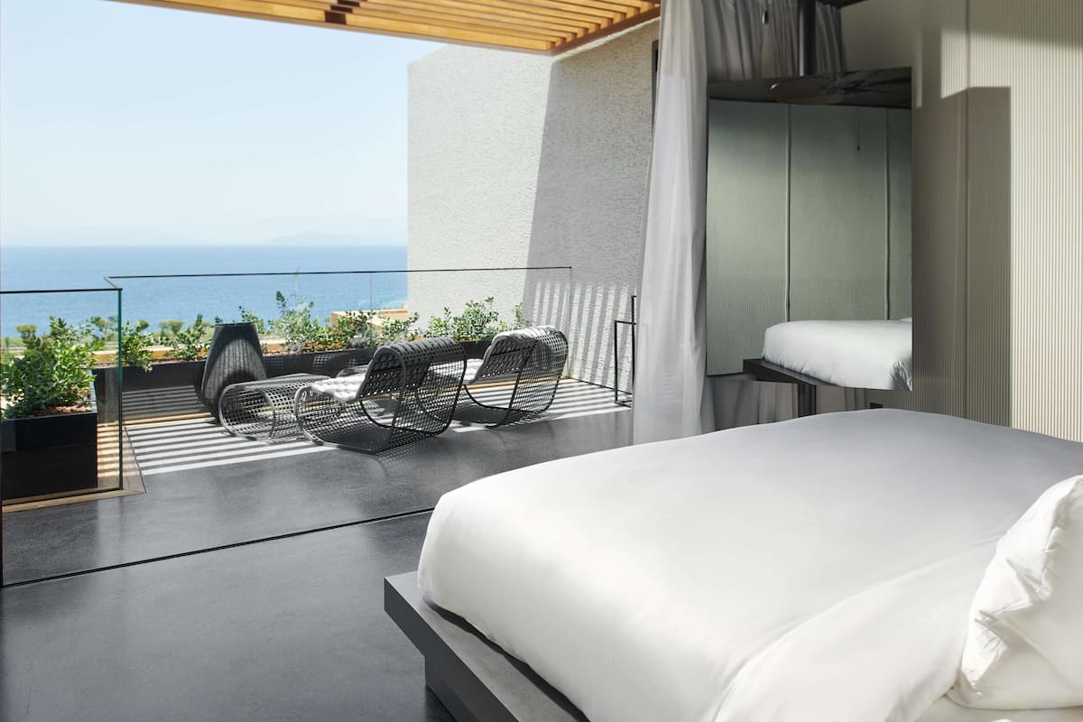 A modern hotel room with a balcony, a bed, and a view of the ocean.