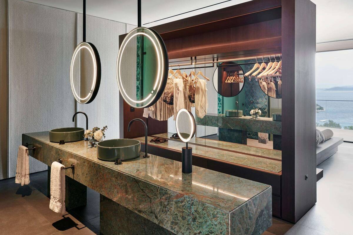A modern bathroom with a large vanity, three mirrors, and a view of the sea.