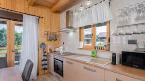 Eine moderne Küche mit Holzschränken, einem Herd und einem Spülbecken. Es gibt hängende Küchenutensilien und ein Fenster mit Vorhängen.
