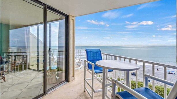 Ein Balkon mit Glastür zu einem Innenbereich, einem kleinen runden Tisch und blauen Stühlen.