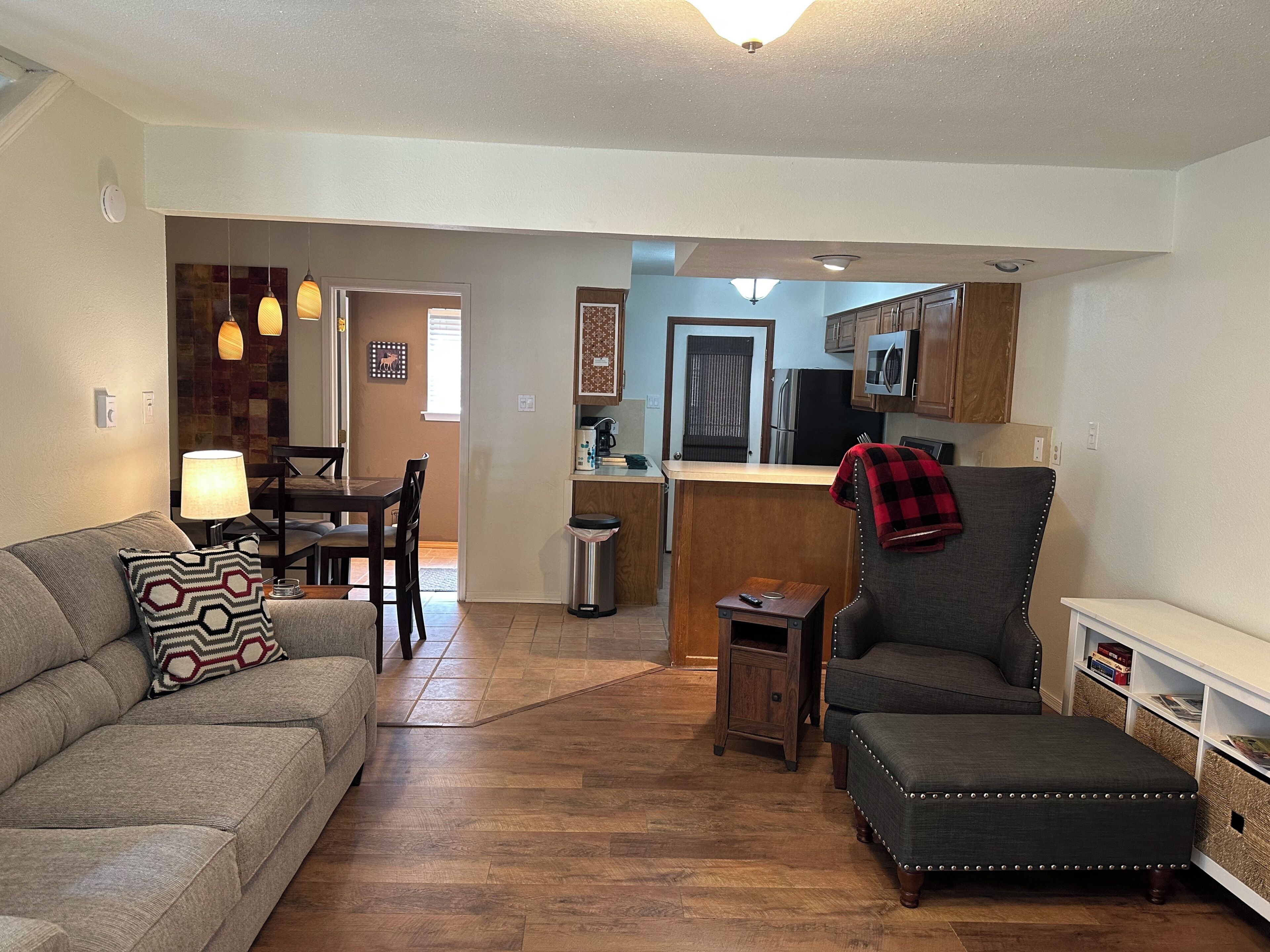A living room with a sofa, a chair, a small table, and a kitchen area with cabinets and appliances.