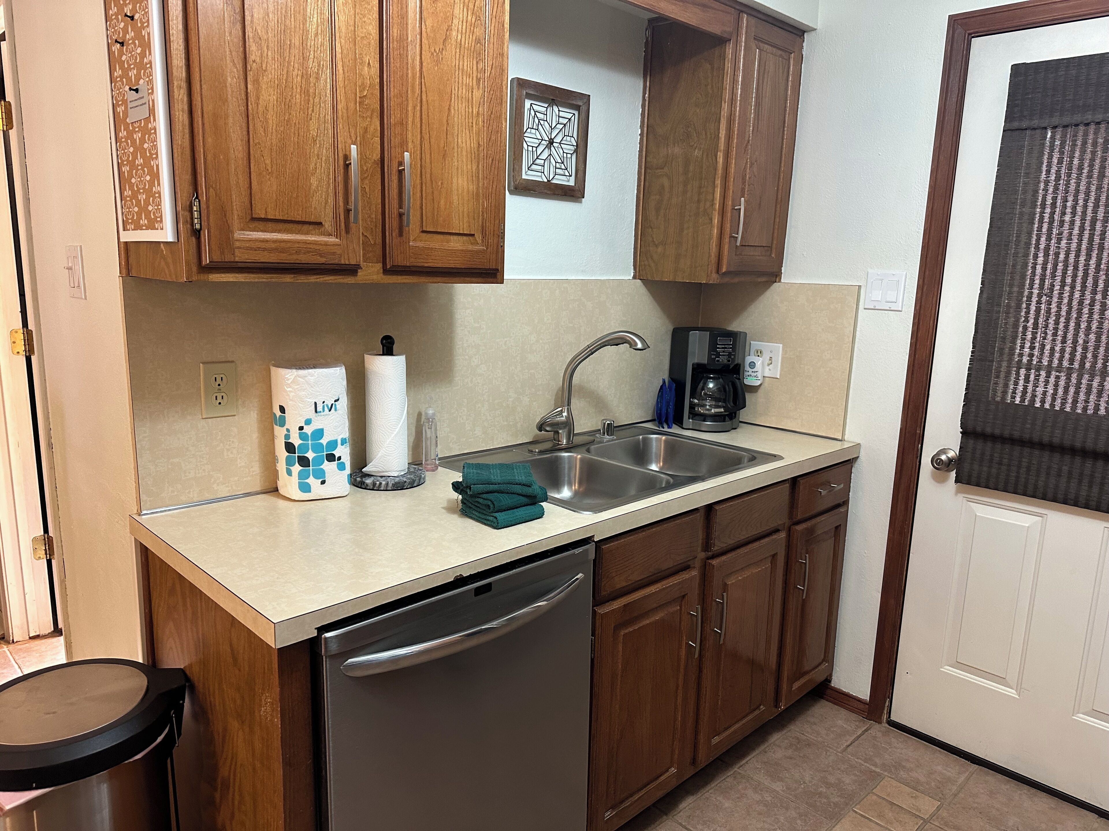 A kitchen with wooden cabinets, a stainless steel sink, a coffee maker, and a dishwasher.
