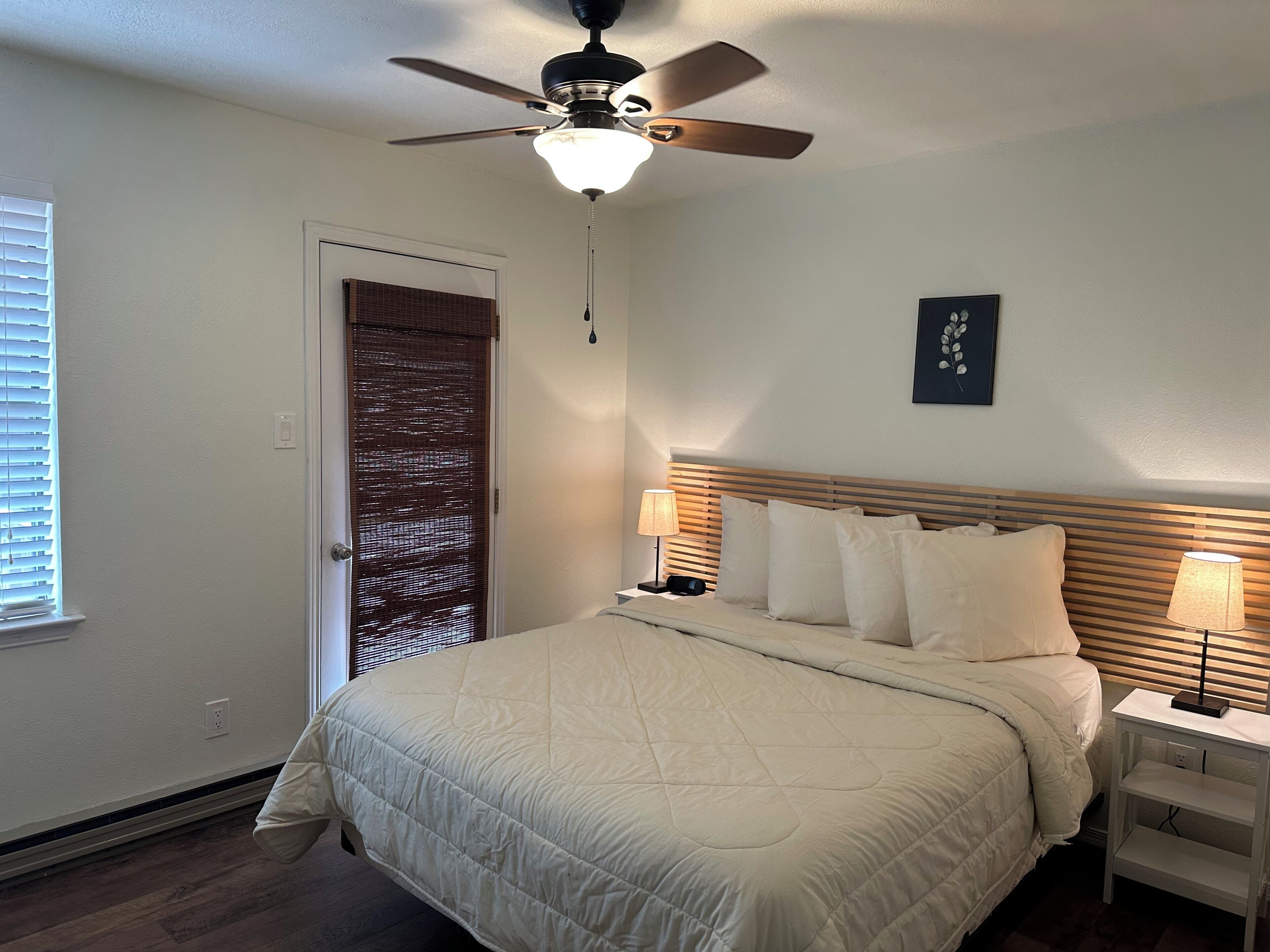 A bedroom with a bed, ceiling fan, bedside lamps, and a door with a window.